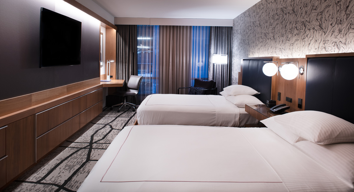 A hotel room with two twin beds, a desk, and a TV on the wall.