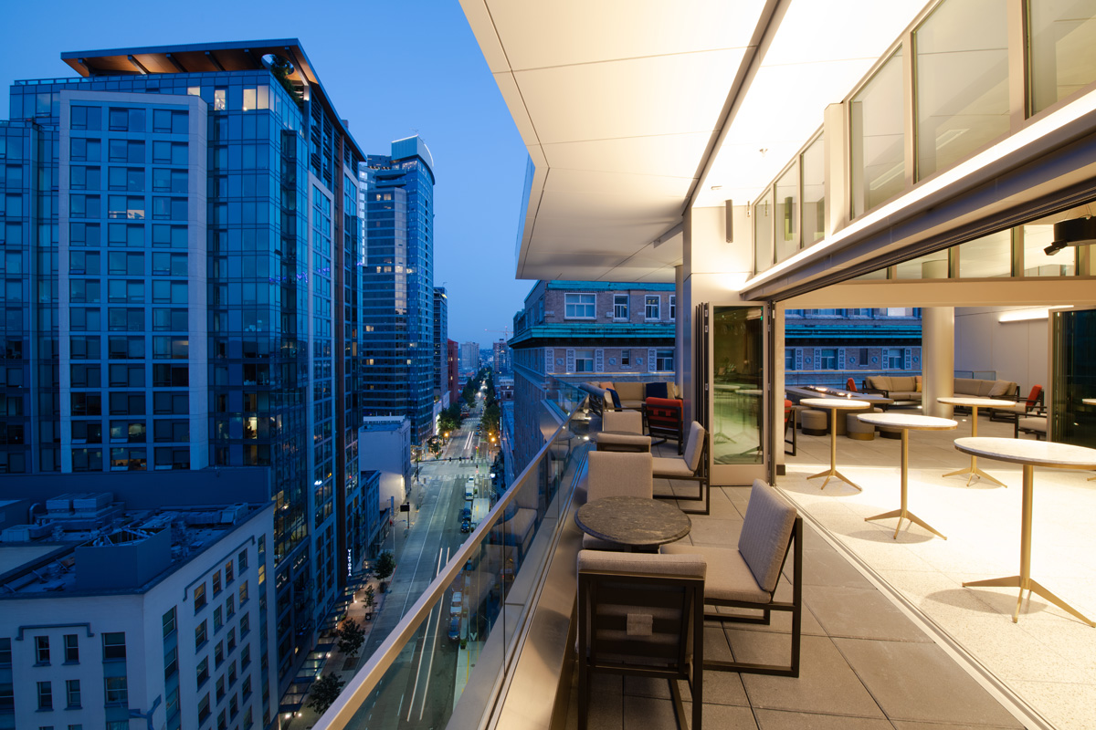 A balcony with modern furniture and a city view at dusk.